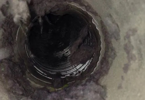 Looking into a dryer vent duct packed with gray lint