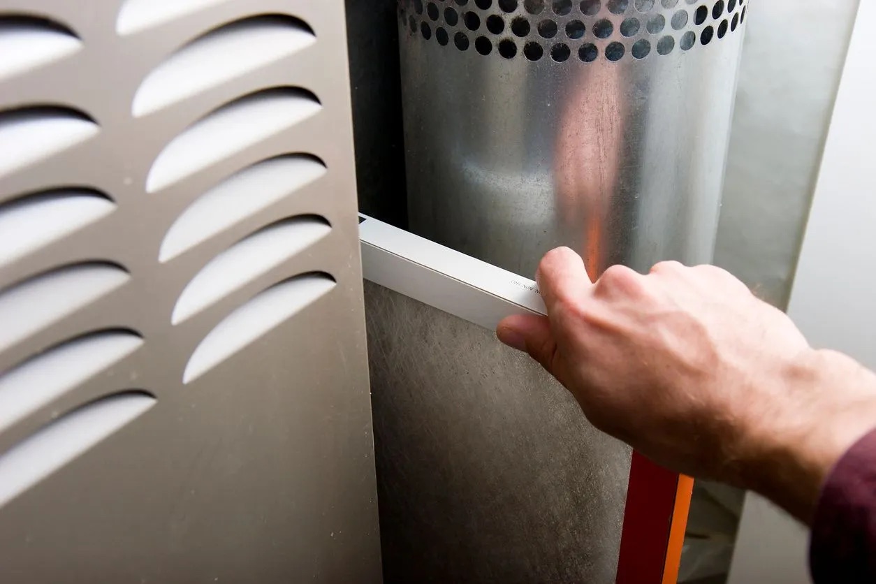 A hand sliding a filter out of a forced-air furnace